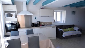 A compact kitchen with a microwave, oven, and coffee maker. There is a dining table with chairs and a sofa with cushions.