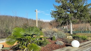 A wooden deck with a garden area featuring a palm tree, a white spherical object, and a wooden post with a light fixture.