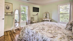 Ein Schlafzimmer mit blumigem Bettbezug, einem Schminktisch, einem Spiegel und einem an der Wand befestigten Fernseher.