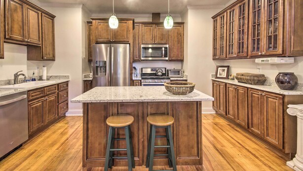 Eine Küche mit Holzausstattung, Edelstahlgeräten, einer Granitabdeckung und zwei Barhocker.