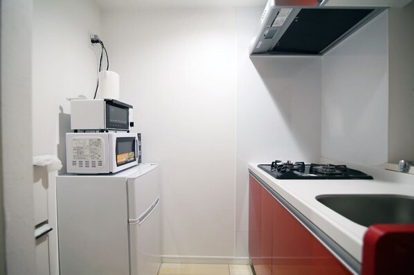 A compact kitchen with a microwave, a small refrigerator, and a gas stove.