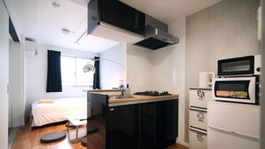 A compact room with a bed, a small kitchenette, and a window with curtains.