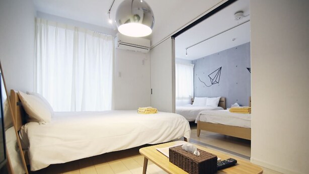 A hotel room with two beds, a wooden table with a basket, a remote control, and a ceiling light.