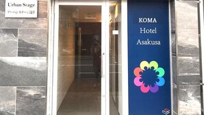 The entrance to KOMA Hotel Asakusa with a sign indicating 'Urban Stage' and a colorful logo on the door.