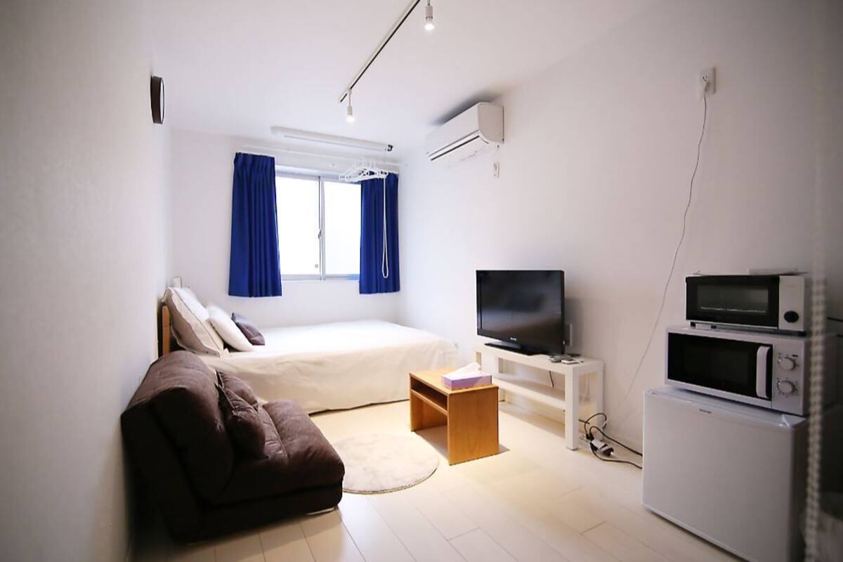 Ein modernes Hotelzimmer mit Bett, Fernseher, Mikrowelle und einer kleinen Sitzecke.