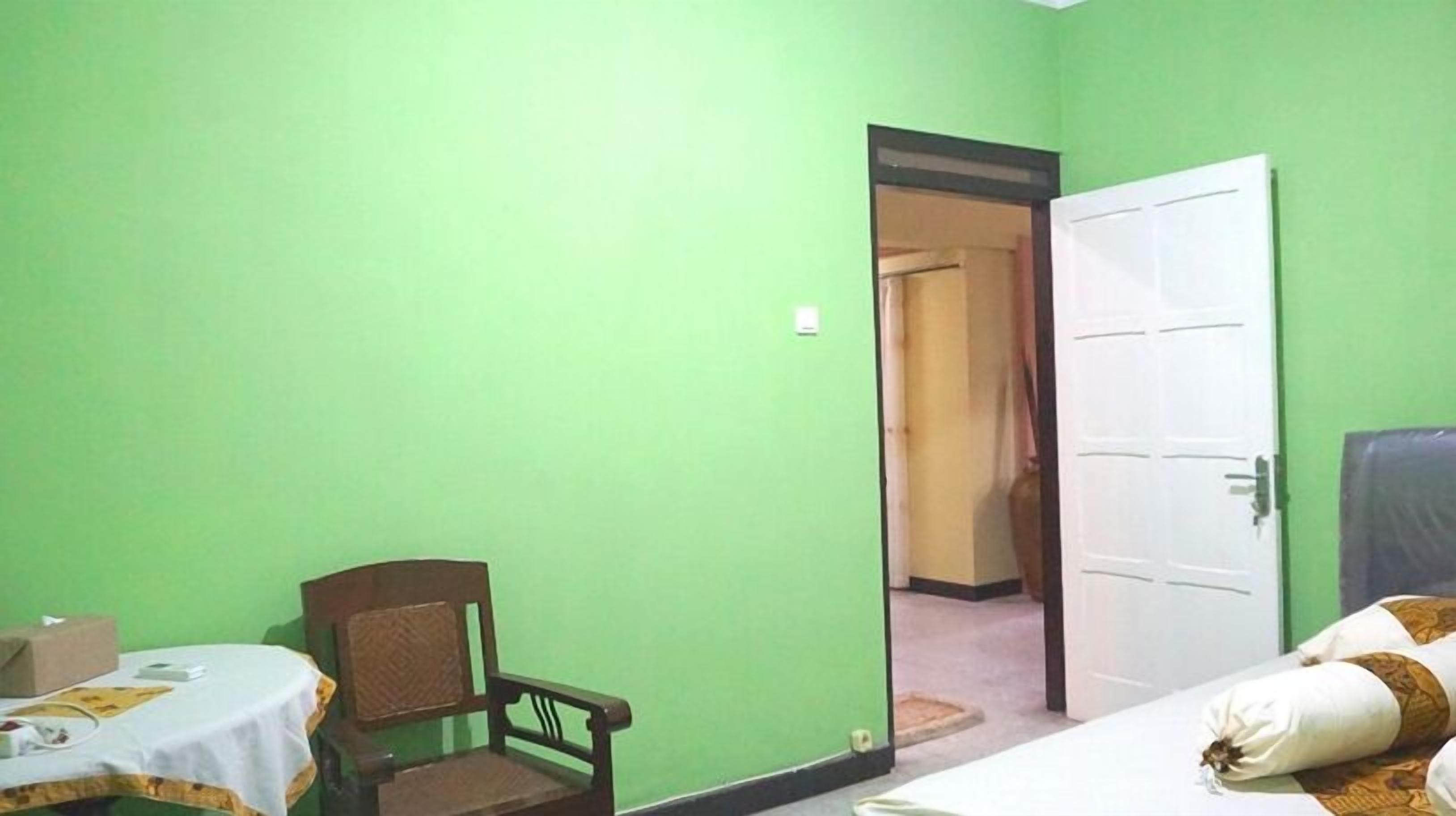 Une pièce aux murs verts, un lit recouvert d’une couvre-lit à motifs, une chaise et une table recouverte d’une nappe blanche.