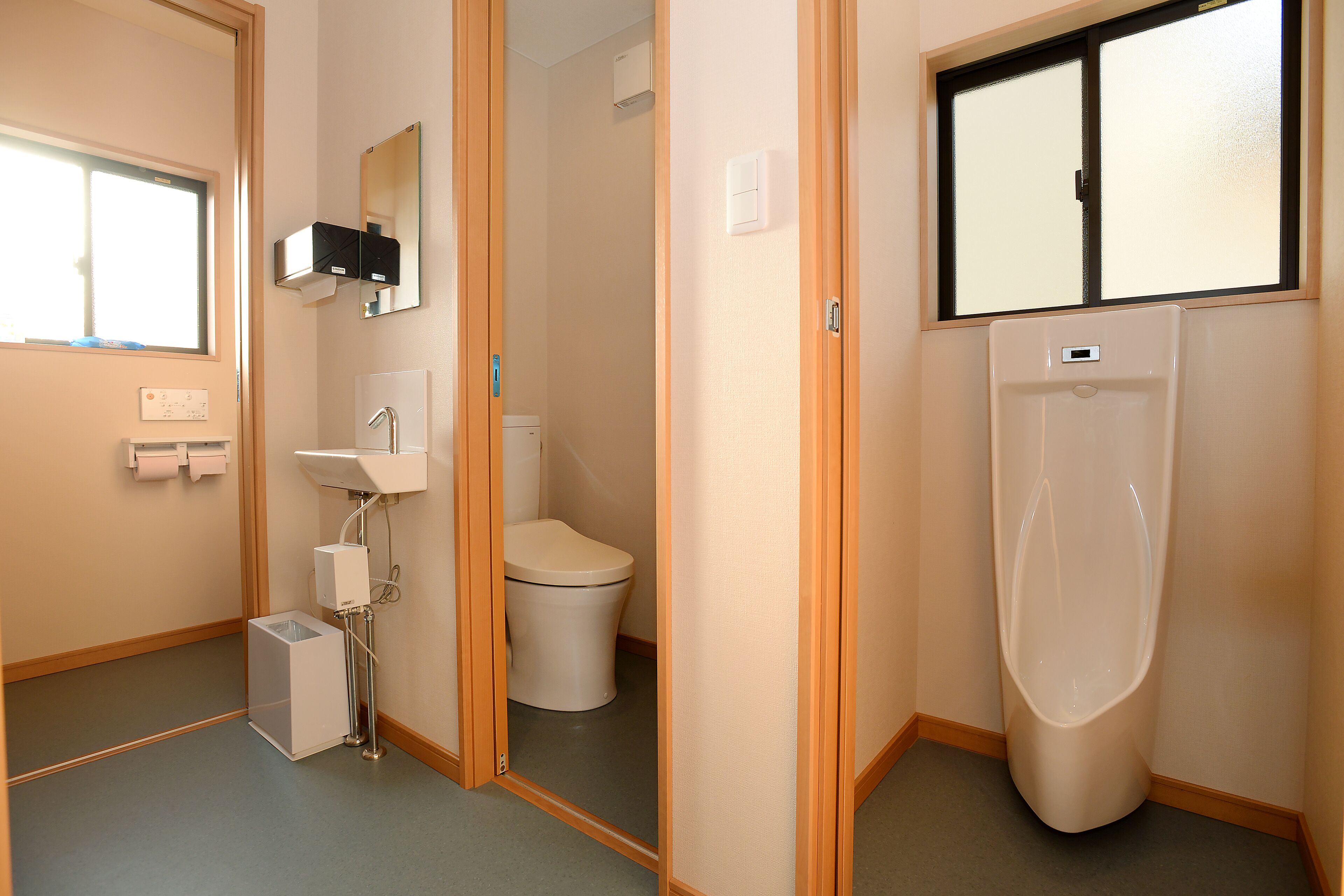 A bathroom with a toilet, urinal, sink, and mirror.