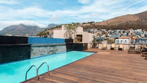A rooftop pool with a wooden deck, a stone wall, and a view of a hillside town. - Unit Number 620 Cape Royale Luxury Apartments (Cape Town)