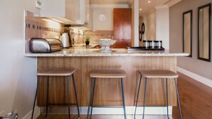 A modern kitchen with a central island, bar stools, a toaster, and a clock on the wall. - Unit Number 620 Cape Royale Luxury Apartments (Cape Town)