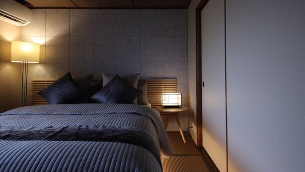 A modern hotel room with a large bed, a bedside lamp, and a small table with a lamp. - Shiki Homes IKKŌ 8 (Kyoto)
