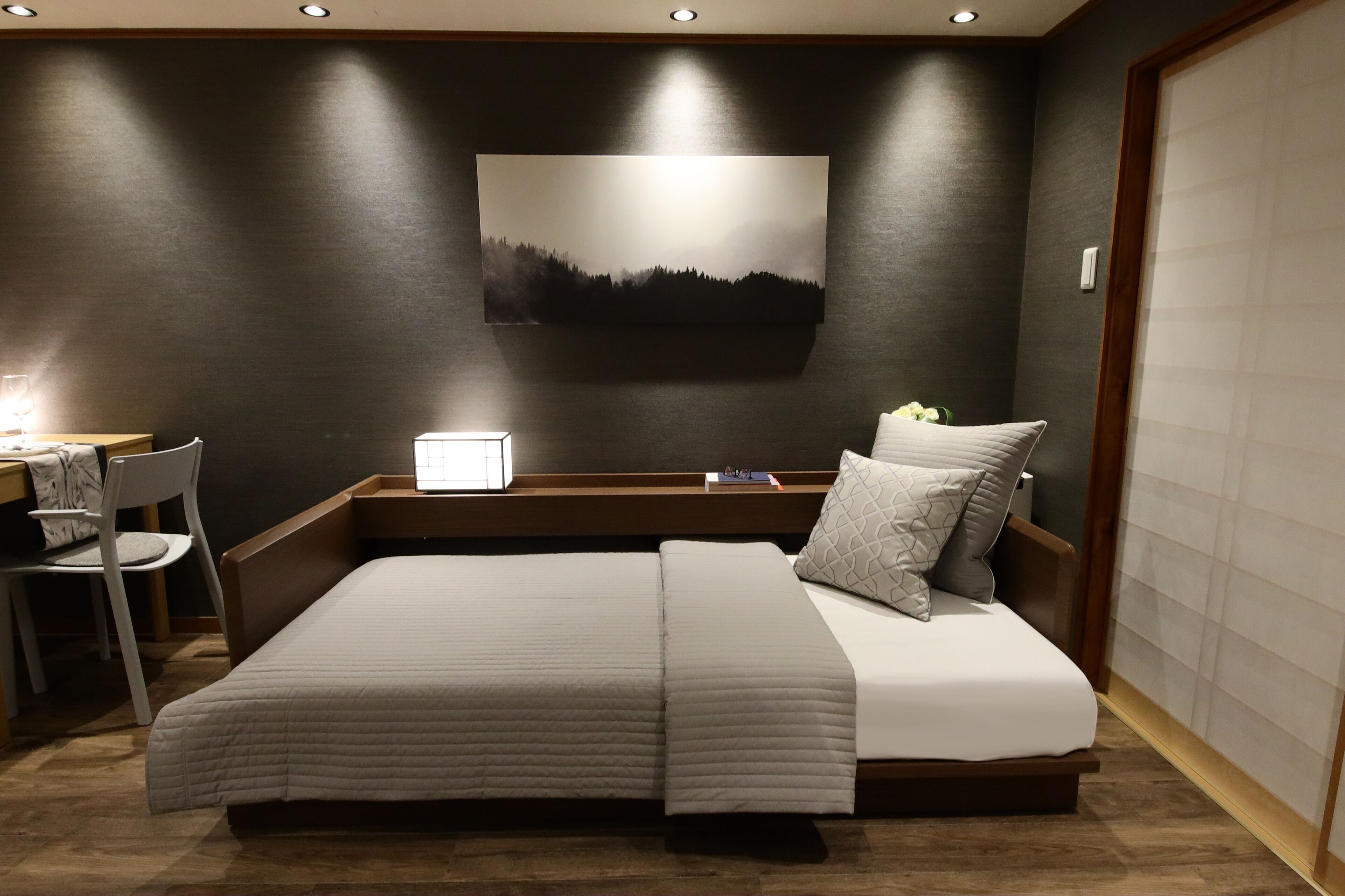 A modern bedroom with a large bed, bedside tables, a chair, and a wall-mounted artwork.