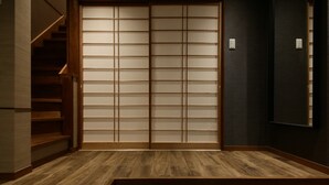 A room with a wooden floor, a sliding door with frosted glass panels, and a dark wall. - Shiki Homes IKKŌ 8 (Kyoto)