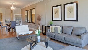 A modern living room with a grey sofa, a glass coffee table, and a dining area with a white table and chairs. - Unit Number 204 Cape Royale Luxury Apartments (Cape Town)