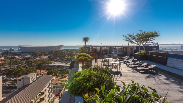 A rooftop terrace with sun loungers, a pool, and a view of the sea and buildings. - Unit Number 204 Cape Royale Luxury Apartments (Cape Town)