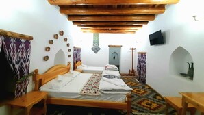 Una habitación con techo de madera, dos camas con colchas estampadas, un televisor y una alfombra con diseño.