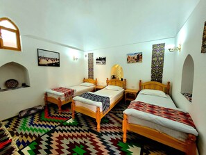 Ein Zimmer mit drei Holzbetten, einem gemusterten Teppich und verschiedenen Wanddekorationen, darunter Bilder und ein Spiegel.