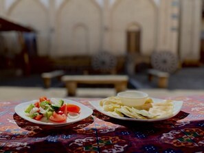 A dining table with a colorful tablecloth, two plates of food, and a bench in the background.