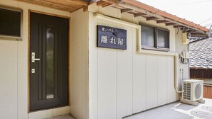 A building with a black door, a sign with Japanese characters, and an air conditioning unit. - Hanareya (Tsushima)