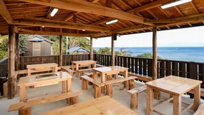 An outdoor wooden deck with picnic tables and benches, overlooking a body of water. - Hanareya (Tsushima)