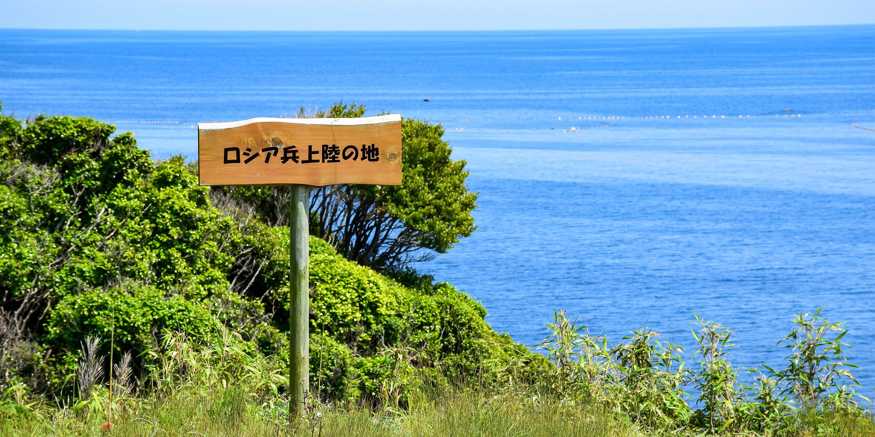 Un letrero de madera con caracteres japoneses en un entorno natural con vista al océano.