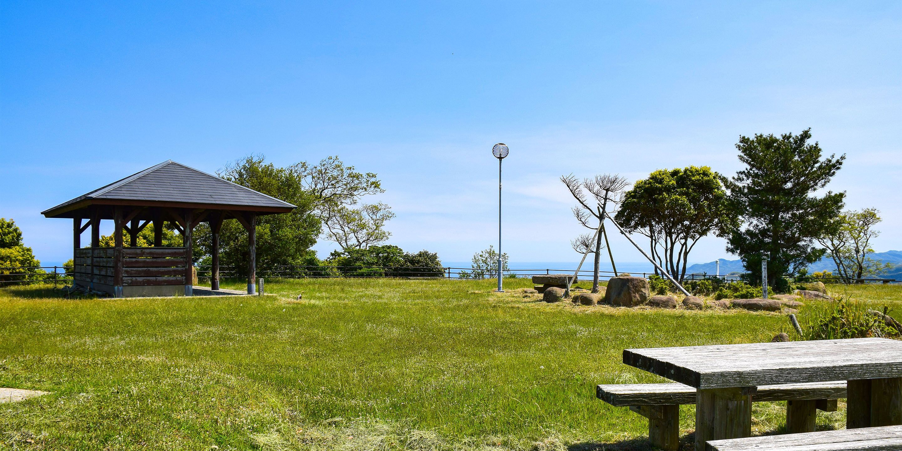 A gazebo, picnic table, and natural landscape with trees and a clear sky.