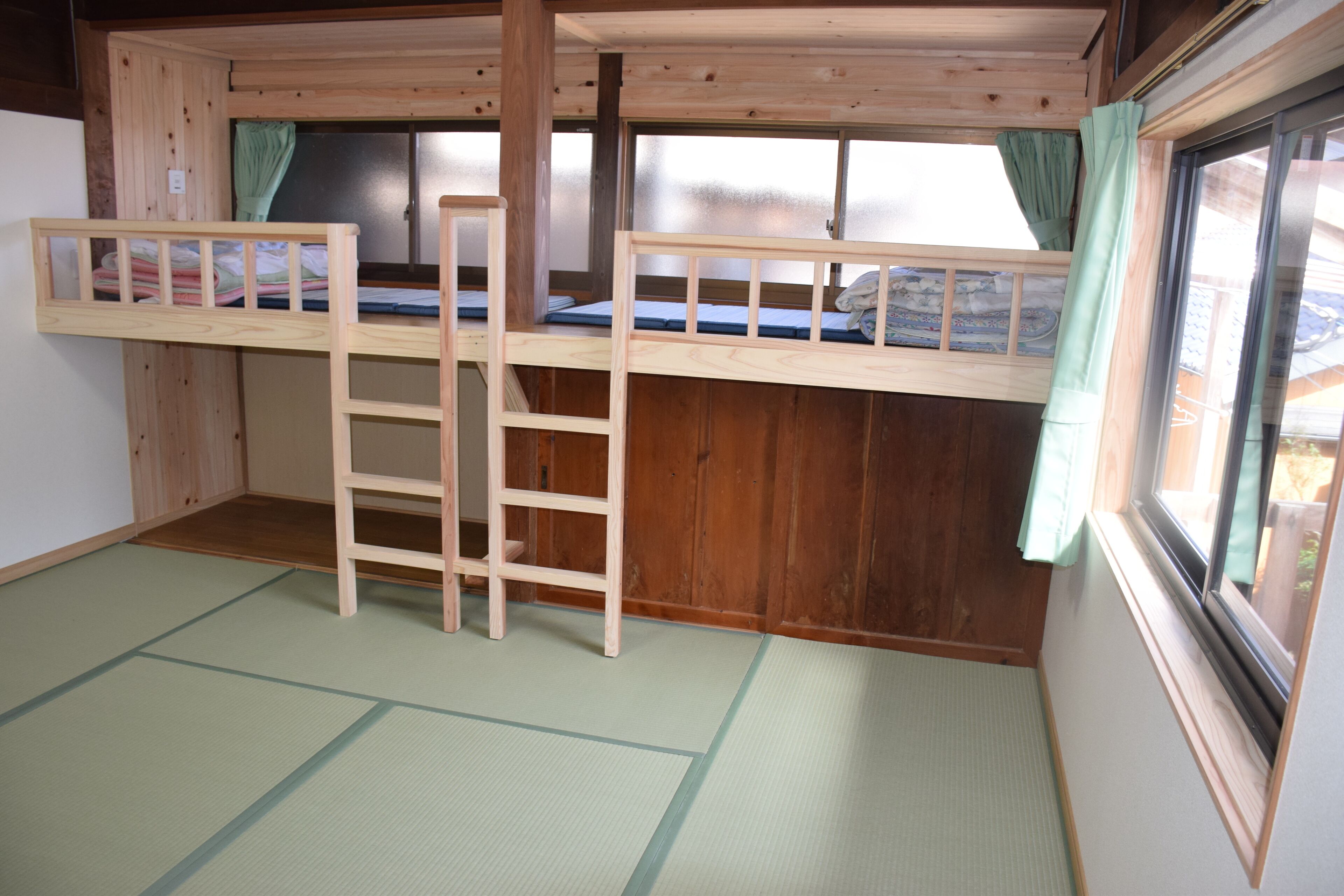 A room with two bunk beds, a ladder, tatami mats, and a window with curtains.