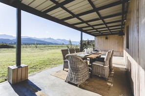 An outdoor patio with a table and chairs, a view of mountains, and a covered area with a wooden wall. - The Farmstead Franschhoek (Franschhoek)