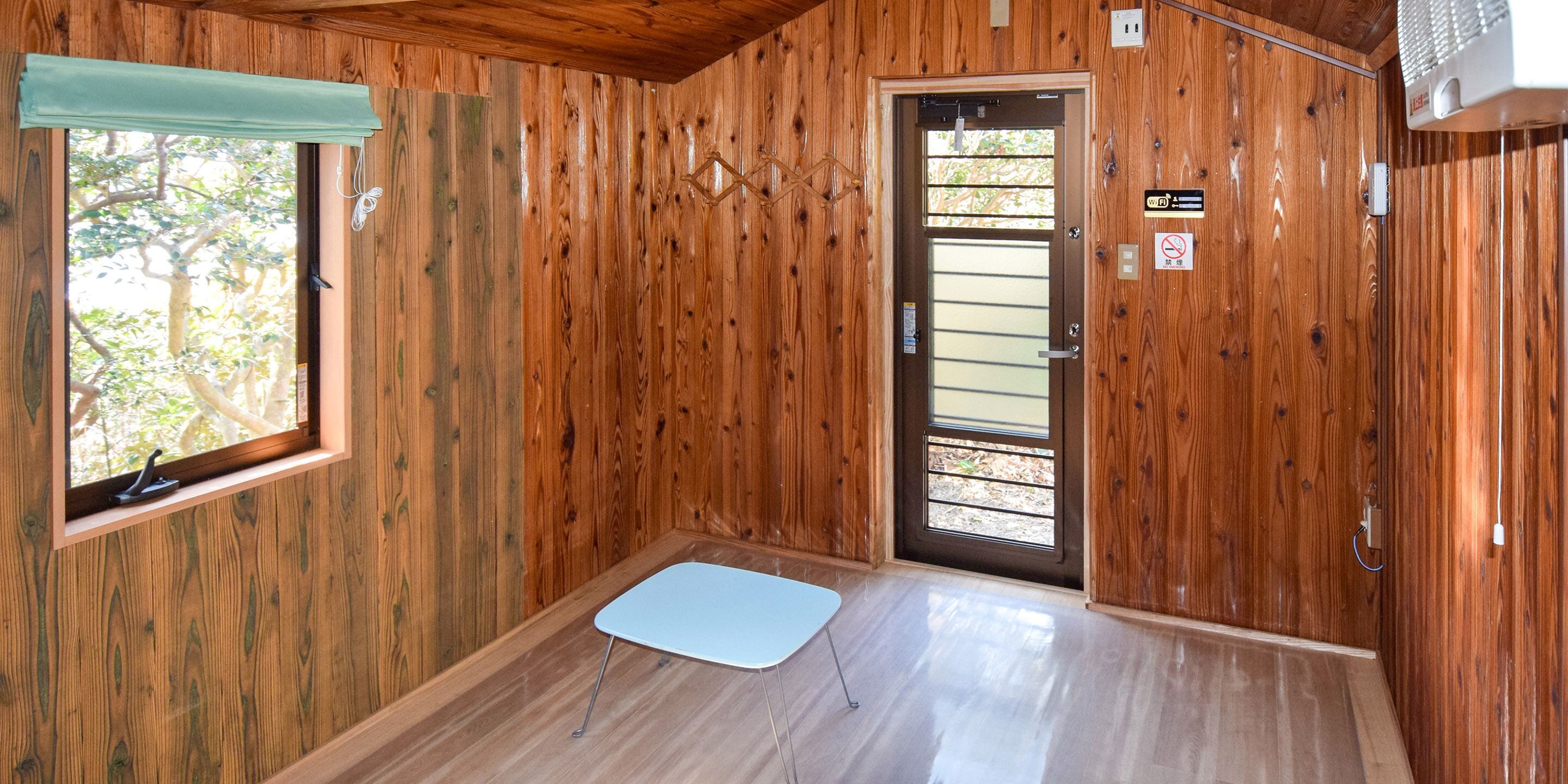 A wooden-paneled room with a door, a window, and a small table.