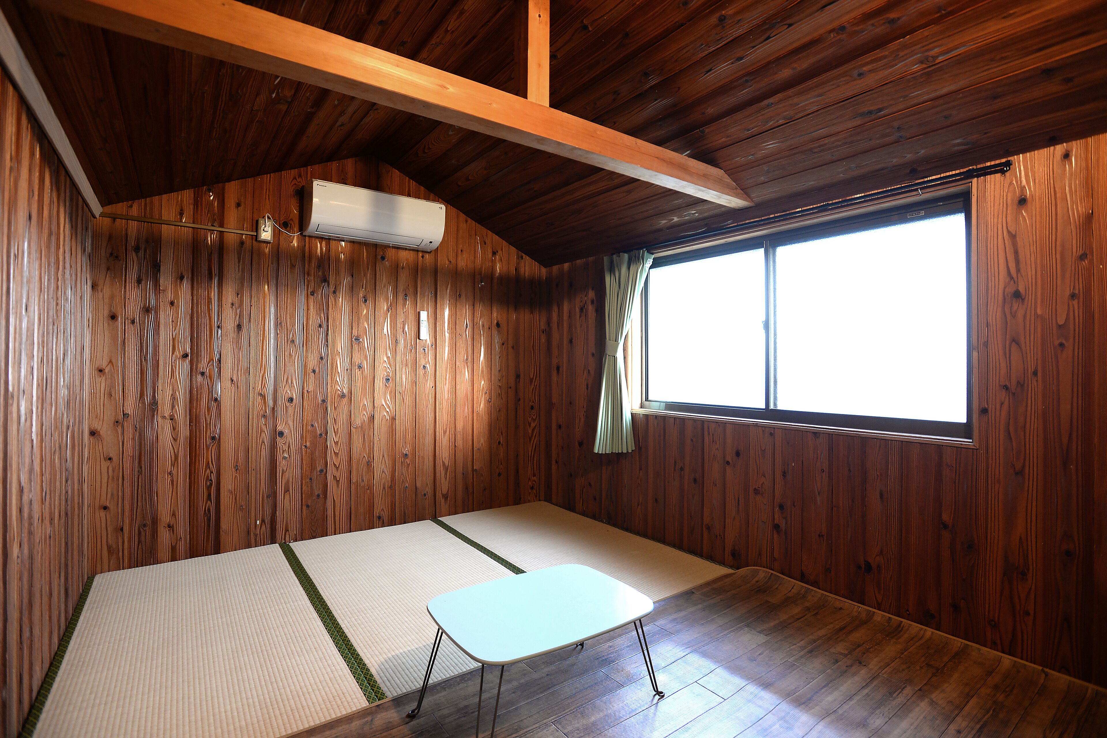 Een kamer met houten wanden, een tatami-mat vloer, een klein tafeltje en een raam met gordijnen.