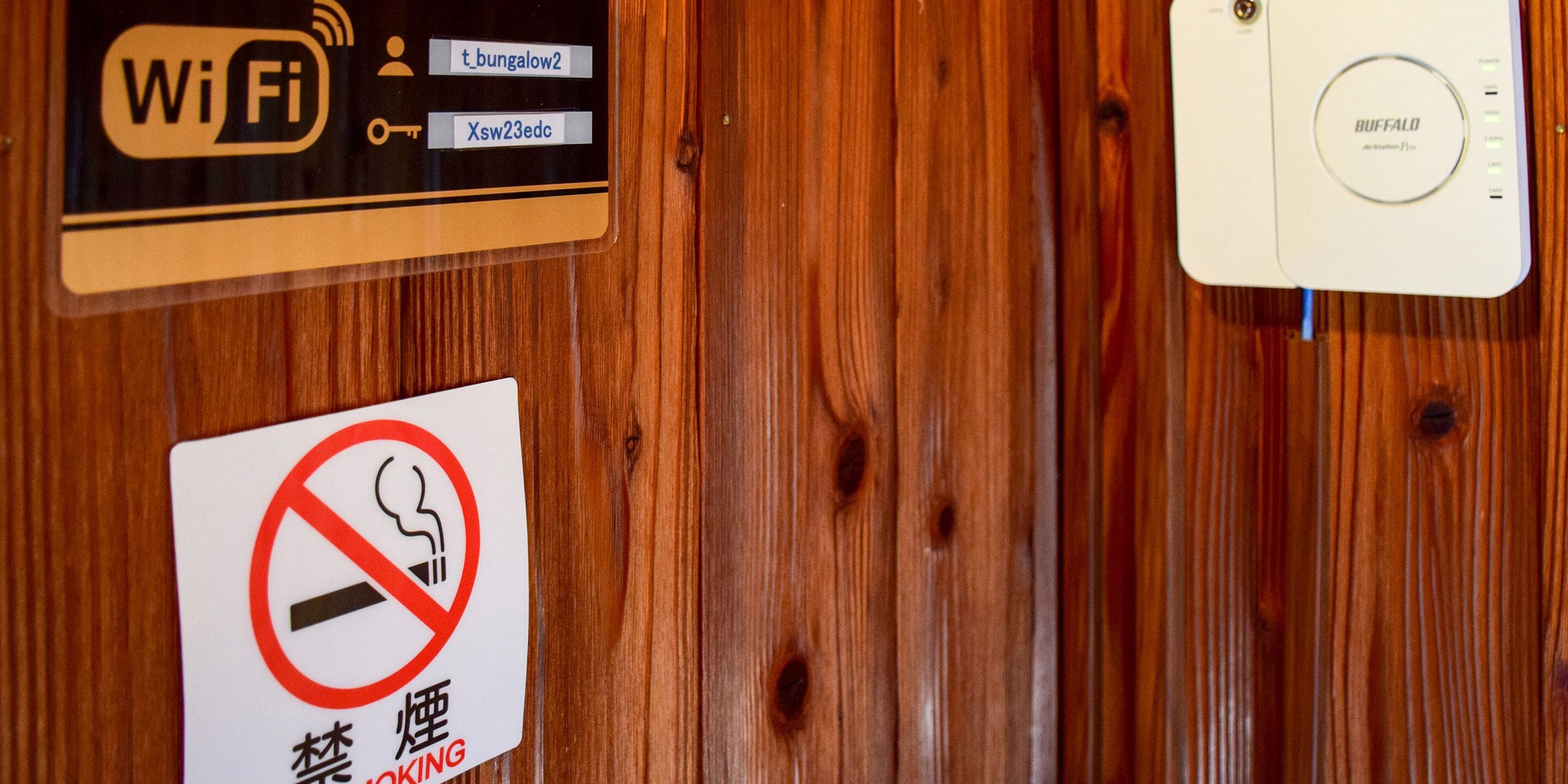 A wooden wall with a Wi-Fi sign, a no-smoking sign, and a Buffalo thermostat.