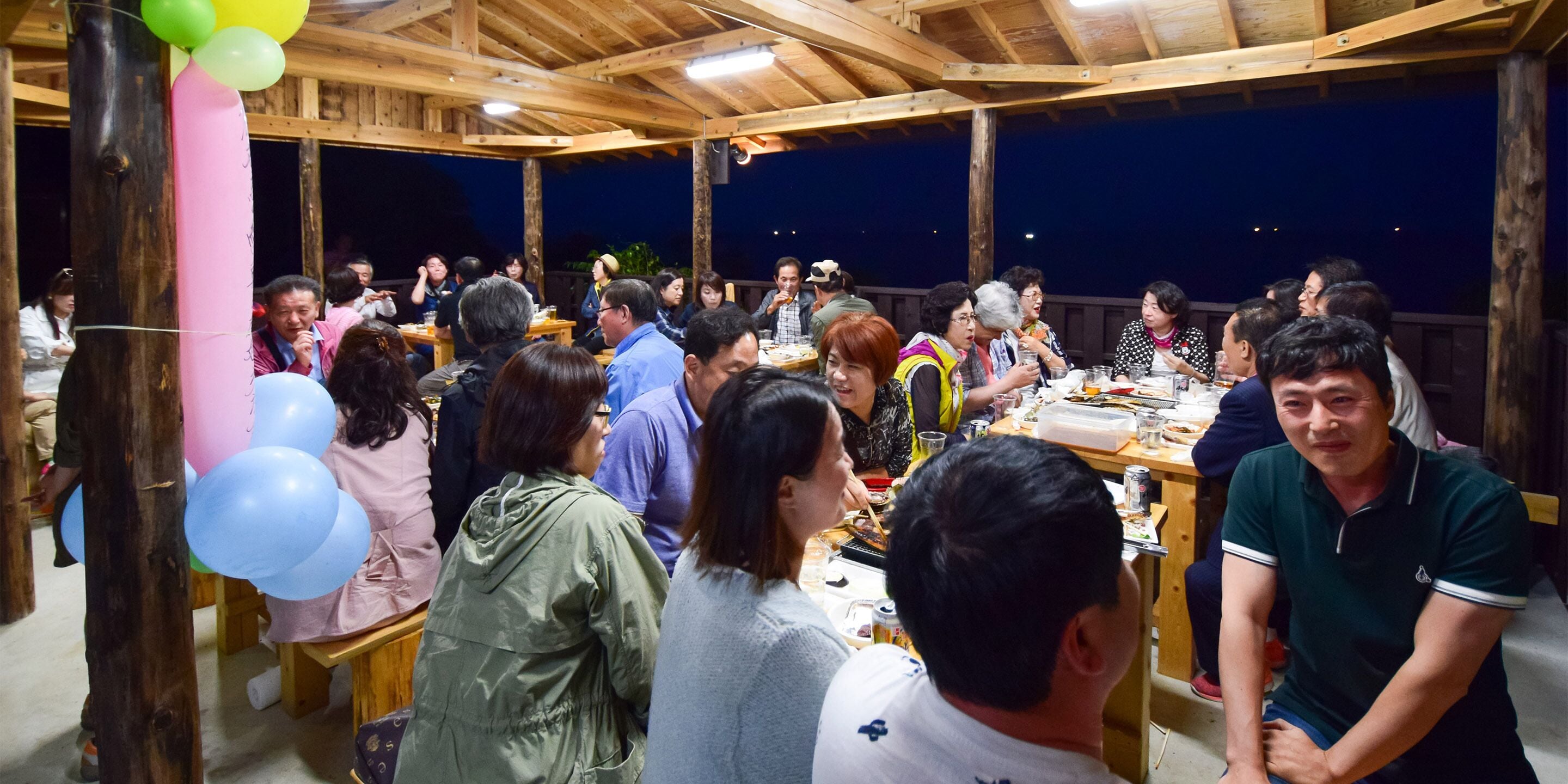 A wooden deck with people dining, featuring a simple table layout and natural lighting.