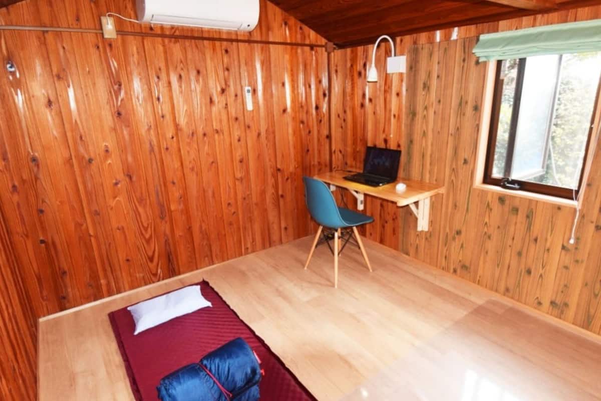 Ein Zimmer in einer Holzhütte mit einem Bett, einem Schreibtisch und einem Stuhl.