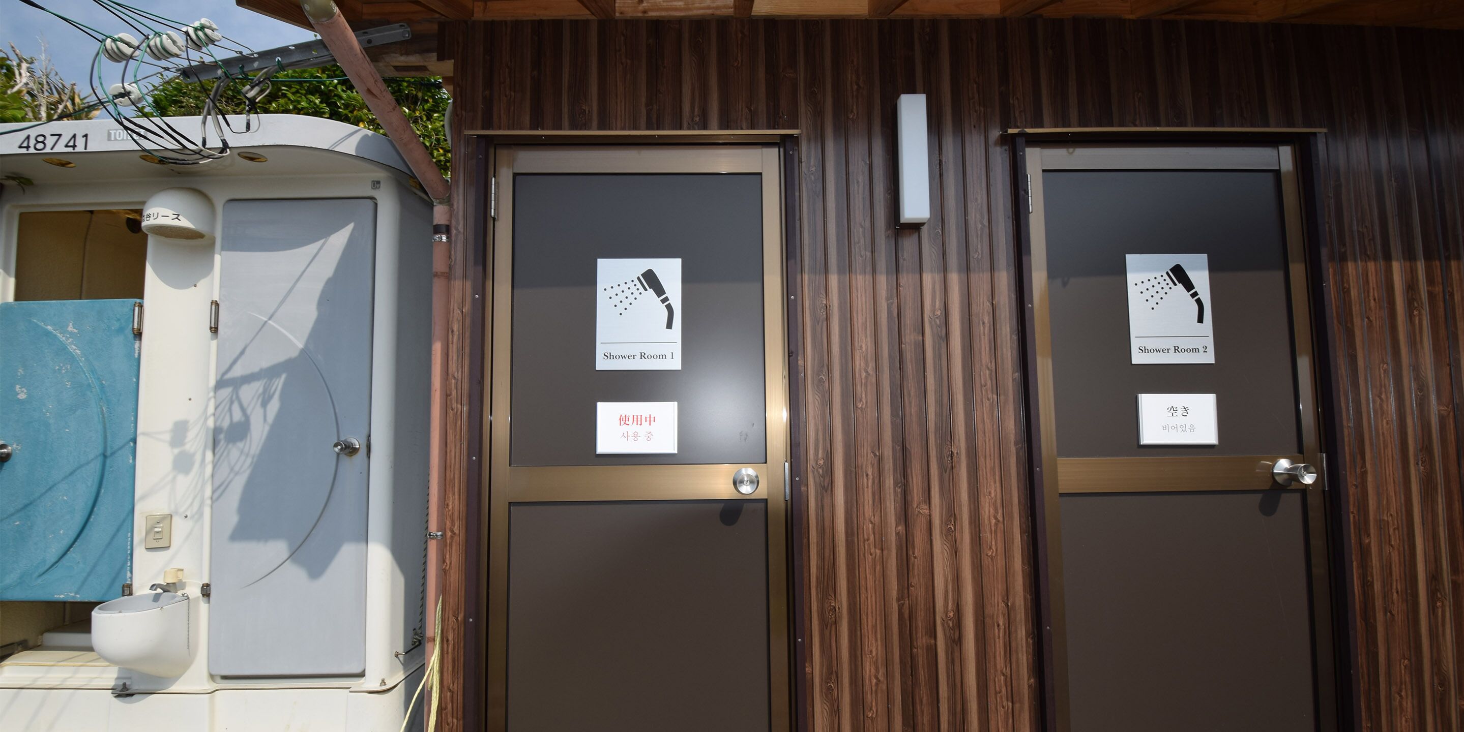 Deux portes en bois, portant les inscriptions « Salle de douche 1 » et « Salle de douche 2 », avec une petite pancarte au-dessus de chaque porte.