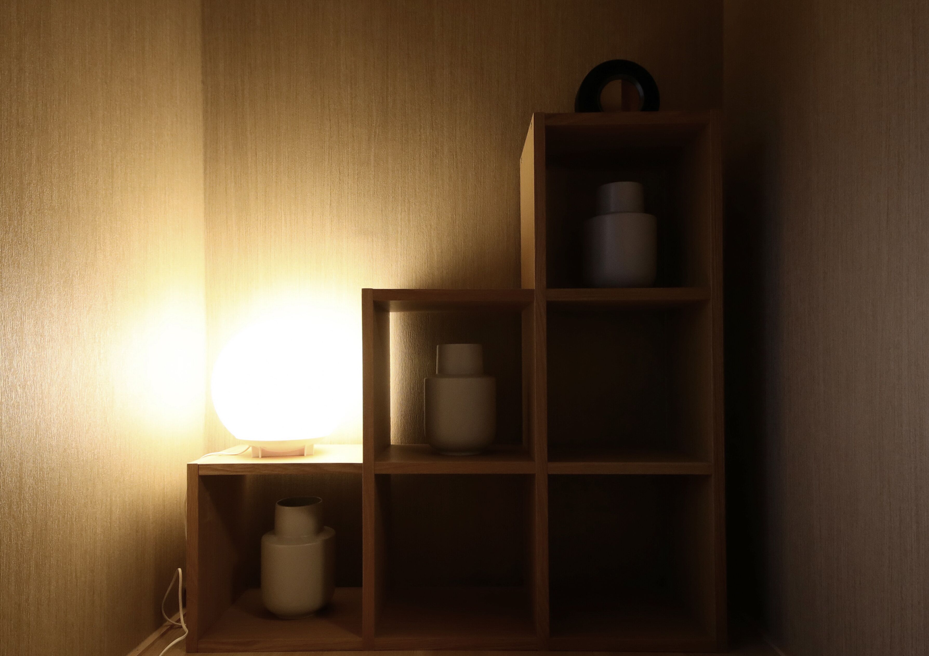 En hylla i trä med tre hyllplan, ett litet bord och en lampa.