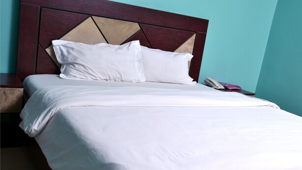 Un lit bien fait, avec du linge de lit blanc et une tête de lit en bois ornée d’un motif géométrique.