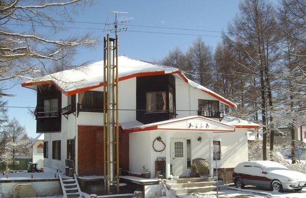 A two-story building with a red and white exterior, a visible front door, and a car parked in front.