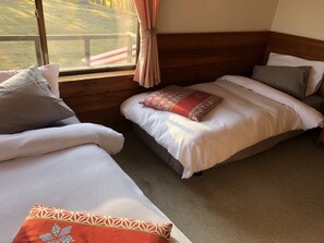 A room with two beds, a wooden headboard, and a window with a view of a grassy area.