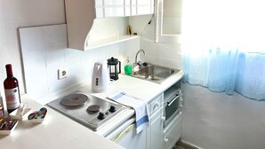 A kitchen with white cabinets, a stainless steel sink, a stove, and a window with a curtain. - Sunflower Apartments & Studios (Corfu)