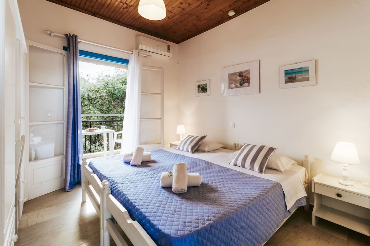 A bedroom with a bed, a nightstand, a window with curtains, and a balcony.
