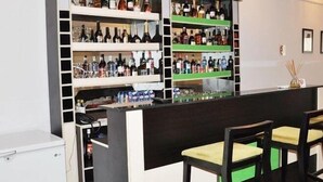 Una zona de bar con estantes llenos de botellas y vasos, un mostrador y dos taburetes de bar.