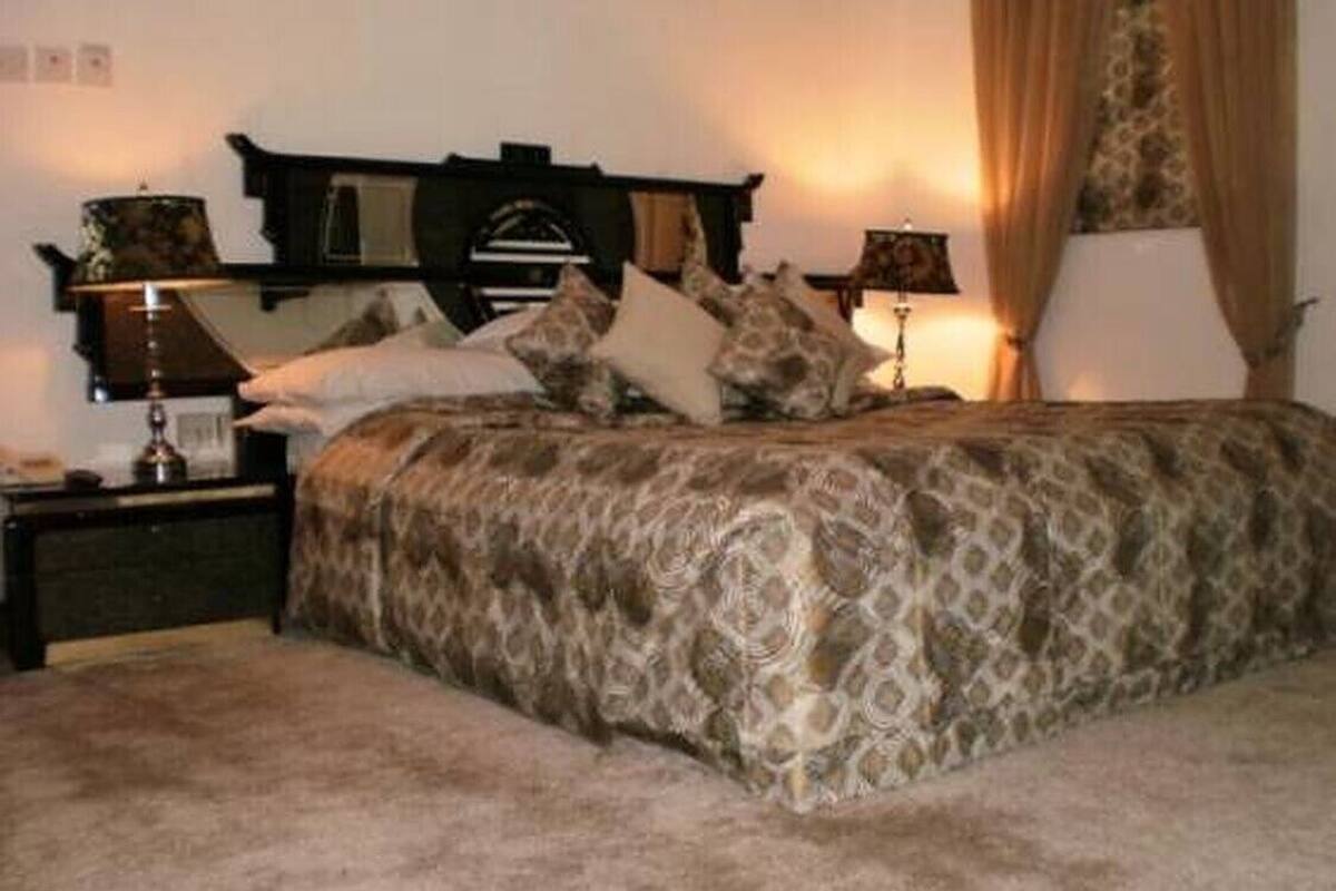 A bedroom with a patterned bedspread, two bedside lamps, a headboard, and a nightstand.