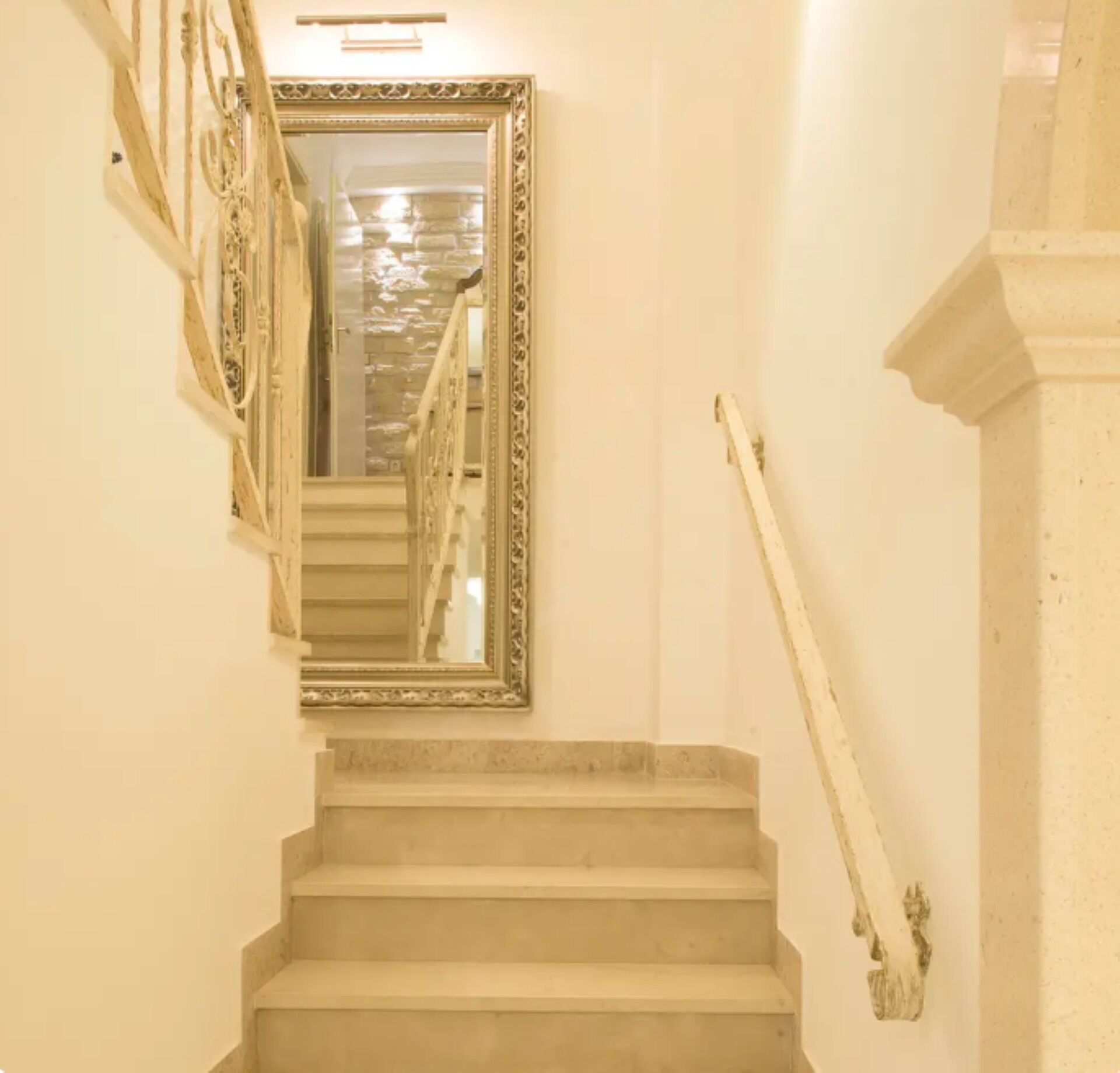 A staircase with a mirror on the wall, leading to a landing with a light fixture.