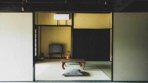 Ein traditioneller japanischer Raum mit Tatami-Boden, einem niedrigen Holztisch, Kissen und einem Fernseher.