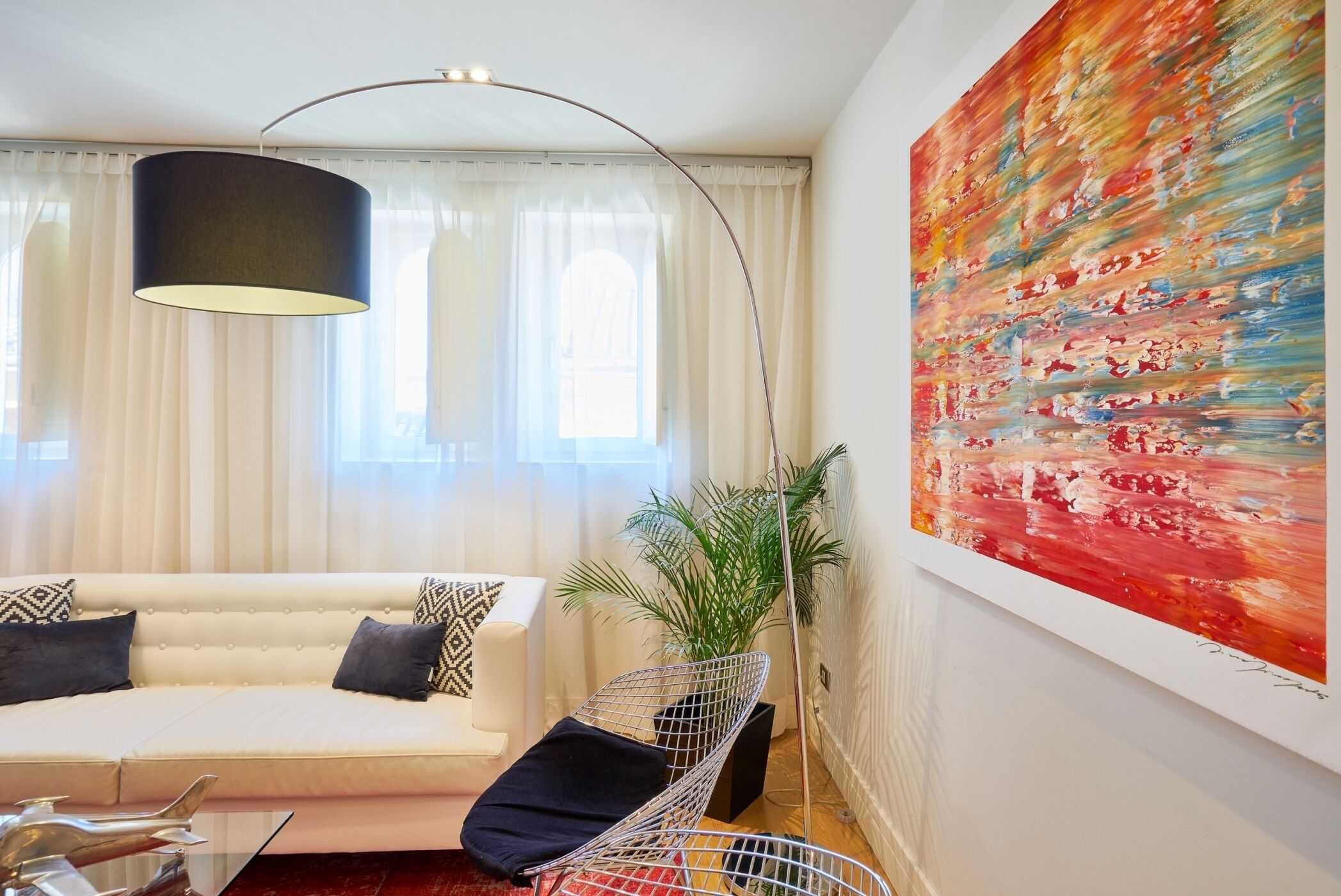 Un salon moderne avec un canapé, une lampe sur pied suspendue, un tableau abstrait aux couleurs vives et une plante en pot.