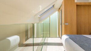 A modern hotel room with a glass partition, a bed with a gray blanket, and a wooden wall. - iloftmalaga Cisneros IV (Málaga)
