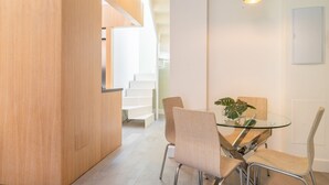 A modern kitchen with a wooden cabinet, a glass dining table with chairs, and a staircase in the background. - iloftmalaga Cisneros IV (Málaga)