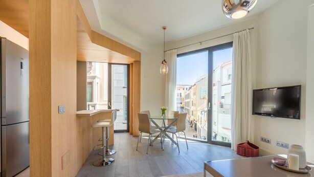 Une chambre d’hôtel moderne dotée d’une cuisine, d’un coin repas et d’une grande fenêtre donnant sur la ville.