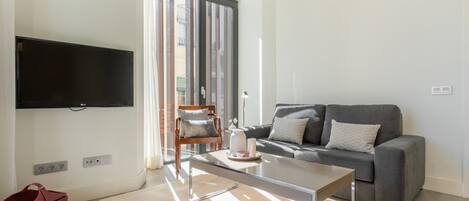 Una sala de estar moderna con un televisor de pantalla plana montado en la pared, un sofá gris con cojines, una mesa de centro de cristal y un mueble de almacenamiento rojo.