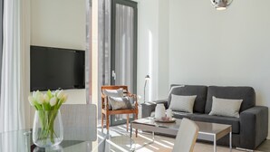 Un salon moderne avec un canapé gris, une chaise en bois, une table basse en verre et un téléviseur à écran plat fixé au mur.