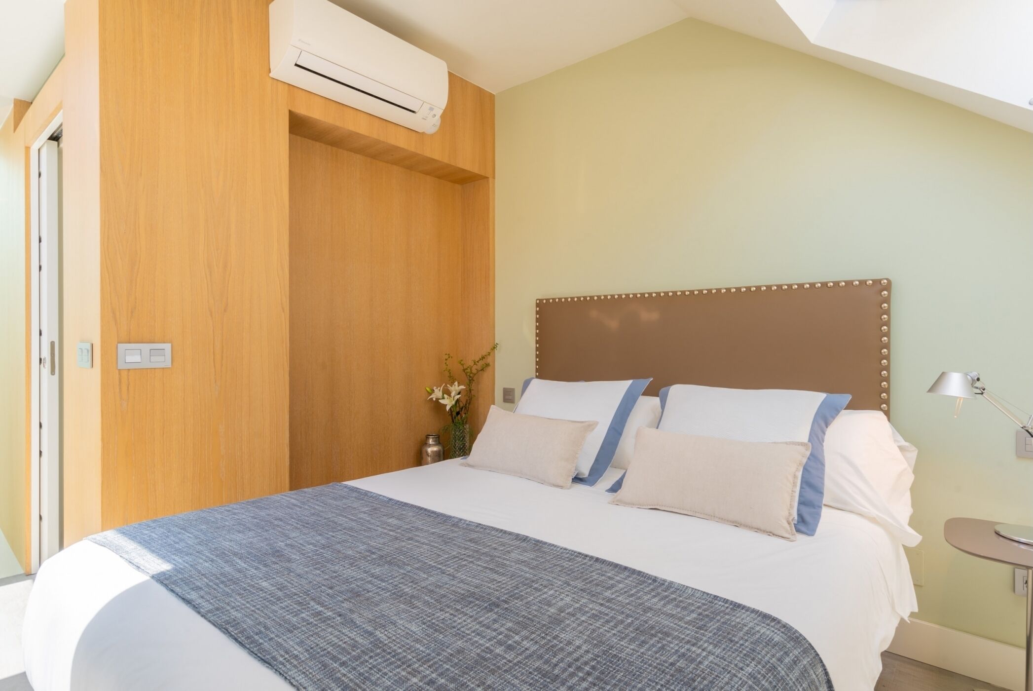 A hotel room with a bed, wooden wardrobe, and a small table with a lamp.